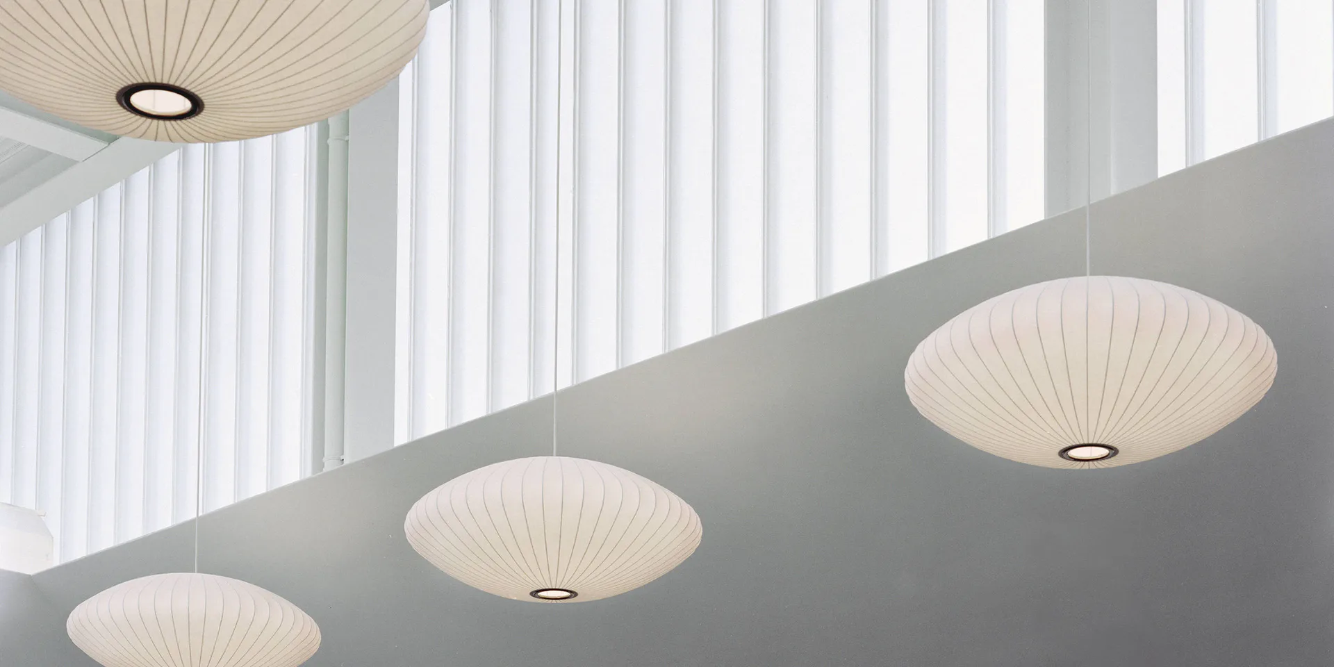 Minimalist ceiling detail with recessed pleated disc lights arranged in a linear pattern against grey soffit and white vertical ribbed panels by Deborah Berke.