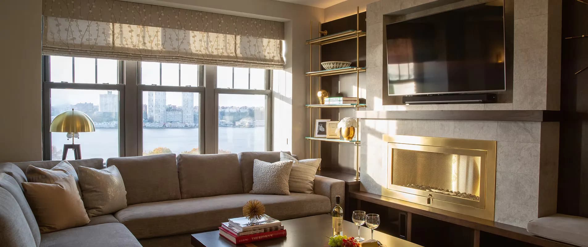 Contemporary living room with sectional sofa, fireplace with built-in shelving, large windows overlooking water, and mounted television by Deborah Emery.