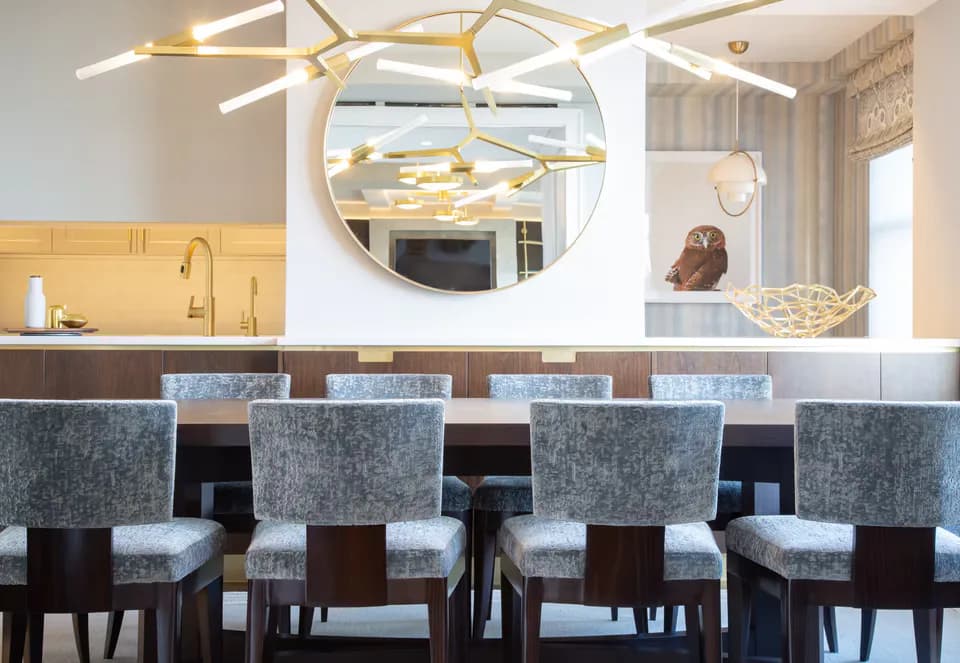Modern kitchen bar with gray upholstered stools, dark wood frames, blue tile backsplash, and circular gold-framed mirror by Deborah Emery.