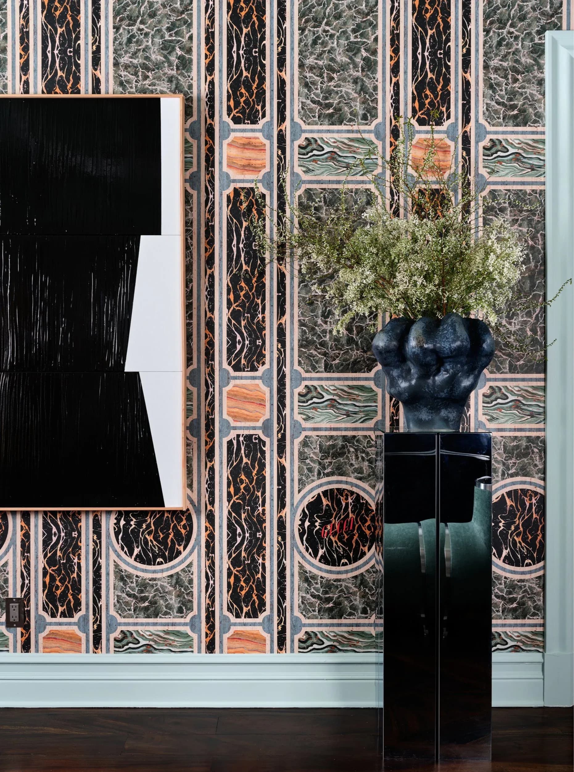 Luxurious interior with ornate patterned wallpaper featuring geometric motifs in black, gold, and green, dark sculptural bust on pedestal, and modern white element by Delia Kenza.