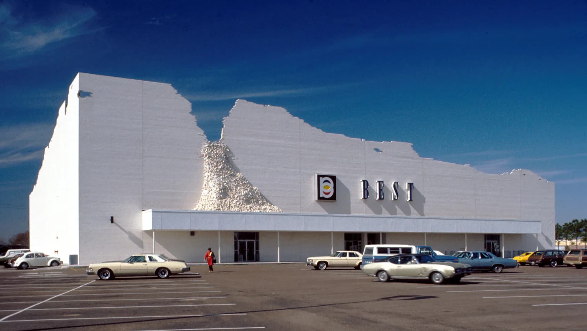 White modernist commercial building with angular geometric forms and a striking pyramidal sculptural element, designed by Denise Mc Lee.