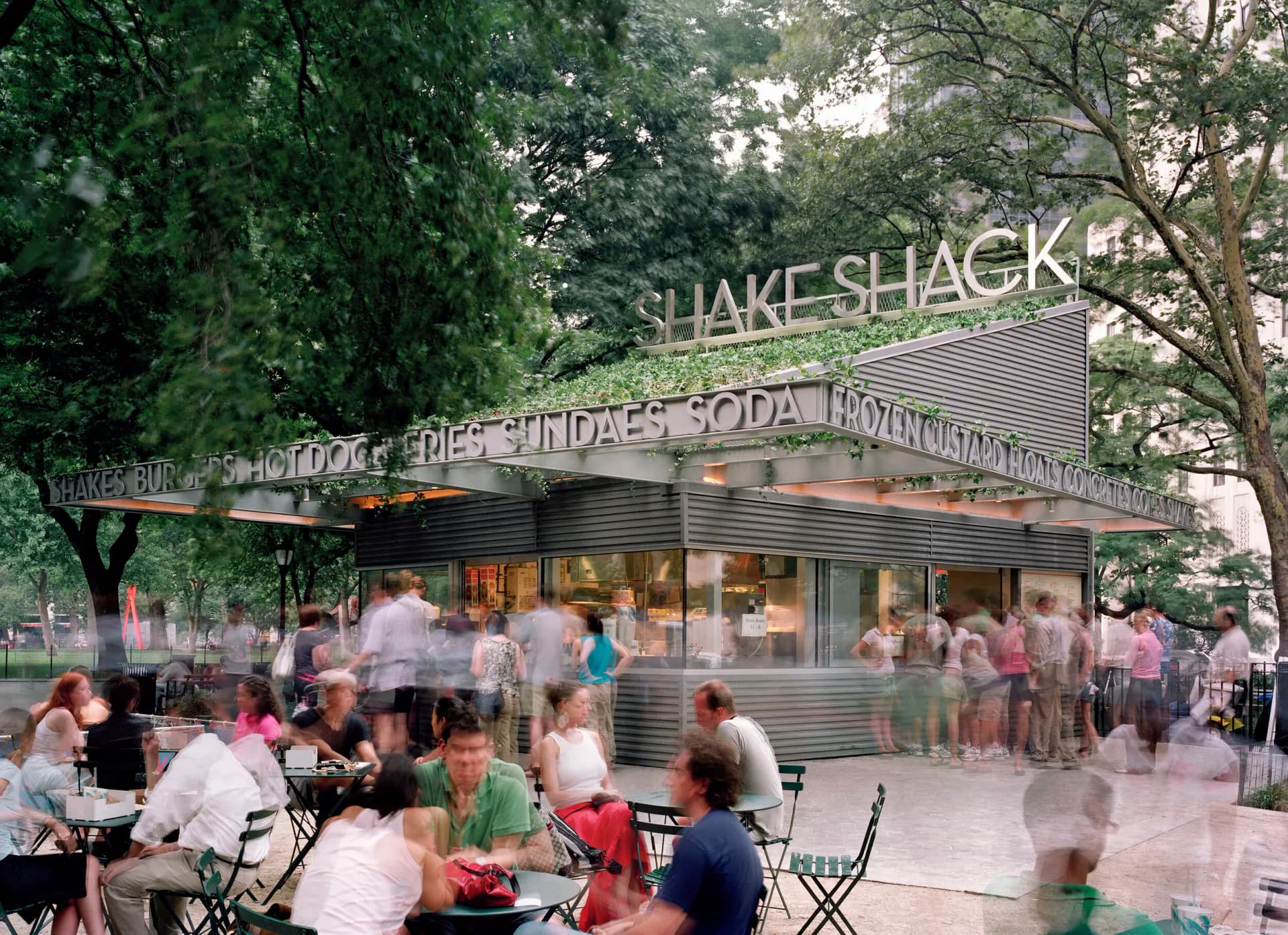 Shake Shack storefront with translucent ghosted figures and trees creating a dreamy, synthetic quality typical of architectural visualization by Denise Mc Lee.