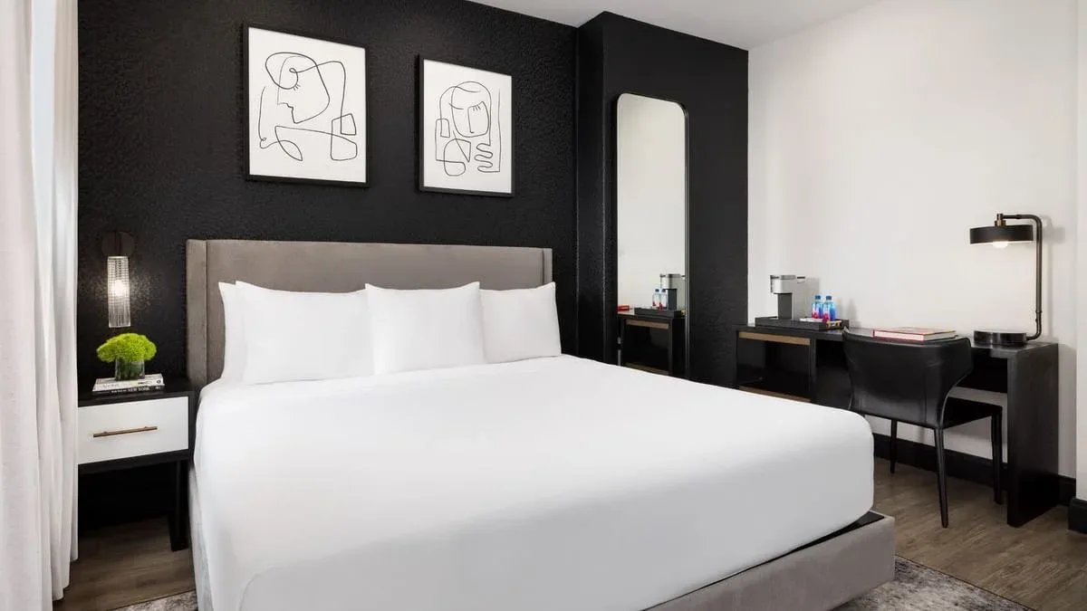 Modern hotel bedroom with black accent wall, white bedding, floating nightstands, and minimalist line art by Derrick Sibley.