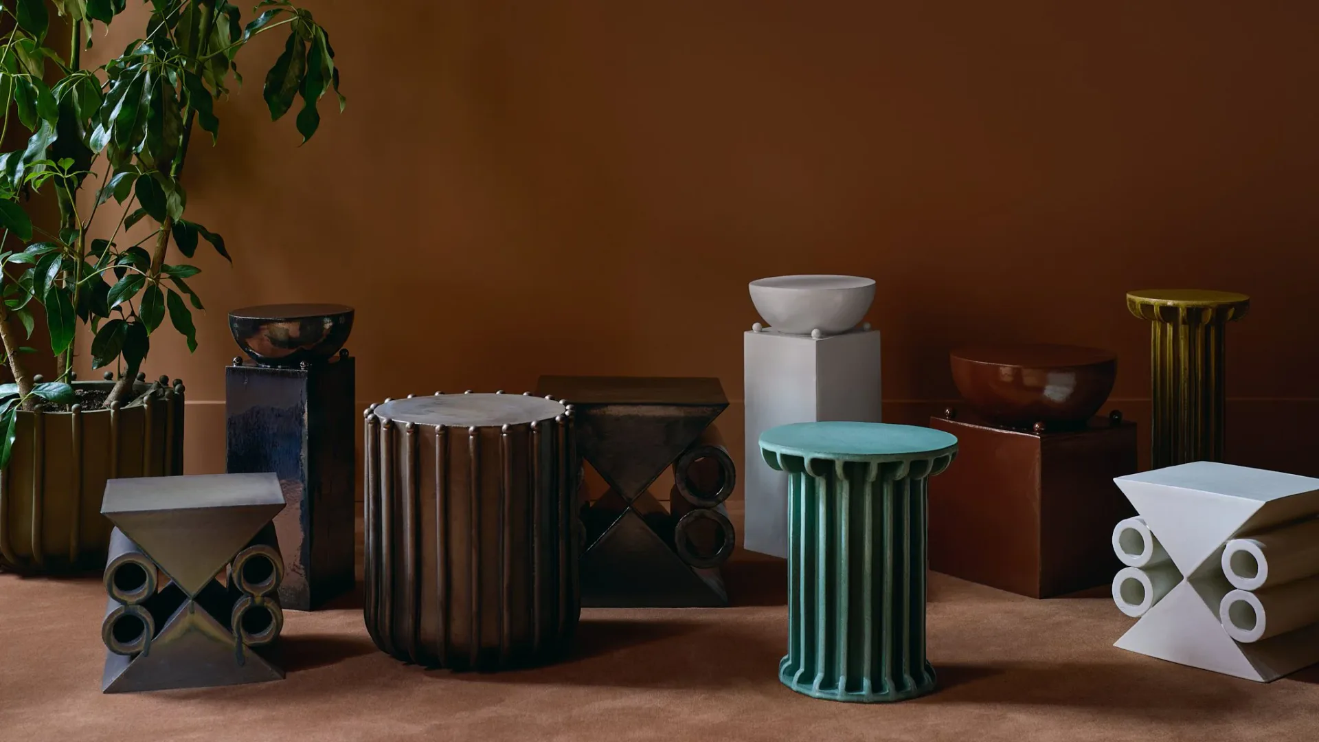 Collection of ceramic and metal vessels with geometric patterns and earth-toned glazes arranged on a terracotta surface by Devin Wilde.