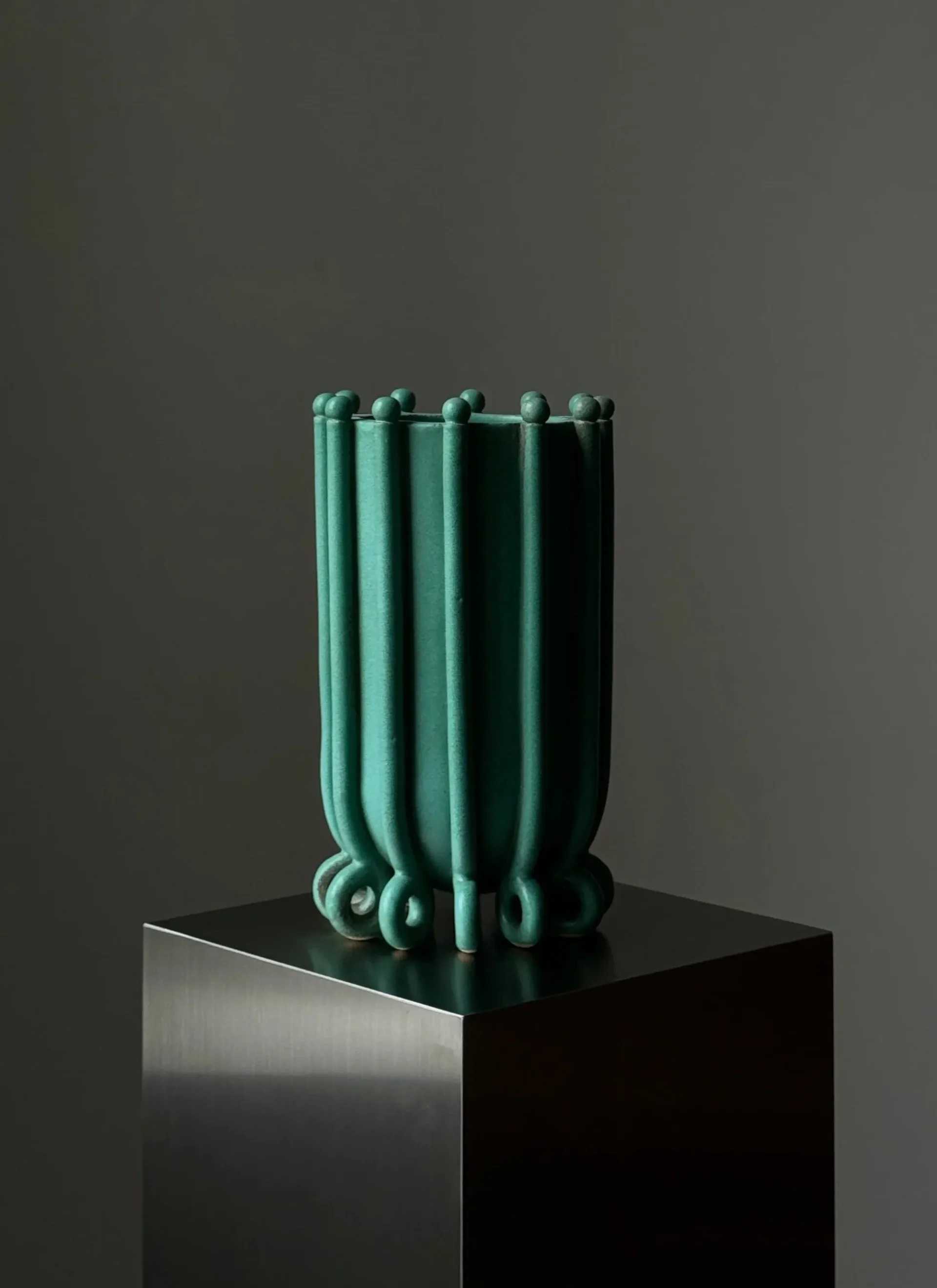 Sculptural installation featuring vertical green-patina metal tubes with spherical elements, displayed on a black plinth by Devin Wilde.