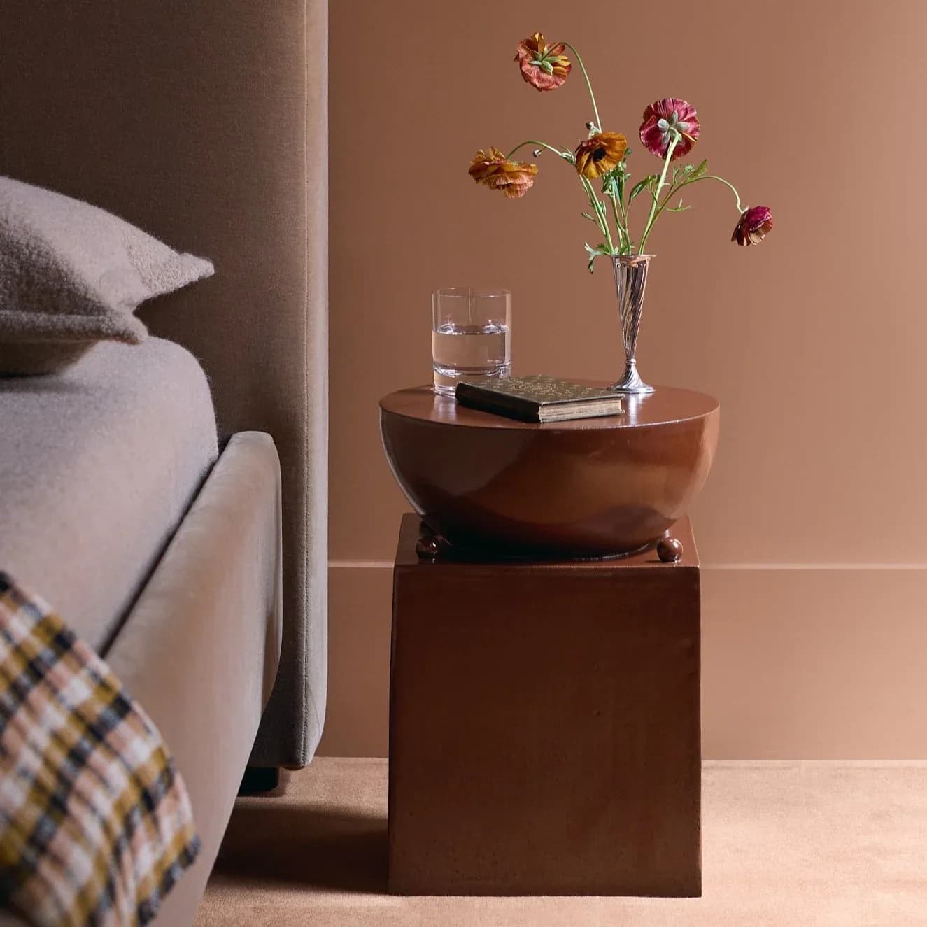 Warm terracotta bedroom interior featuring stacked wooden cube nightstands with a sculptural bowl top, glass vase with colorful flowers, and soft bedding by Devin Wilde.
