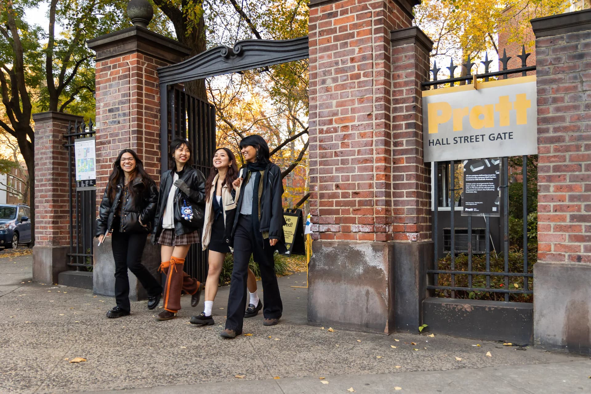 Brick entrance gateway with dark wooden doors and yellow signage for Hall Street Gate, surrounded by autumn foliage, by Diana Azbenova.