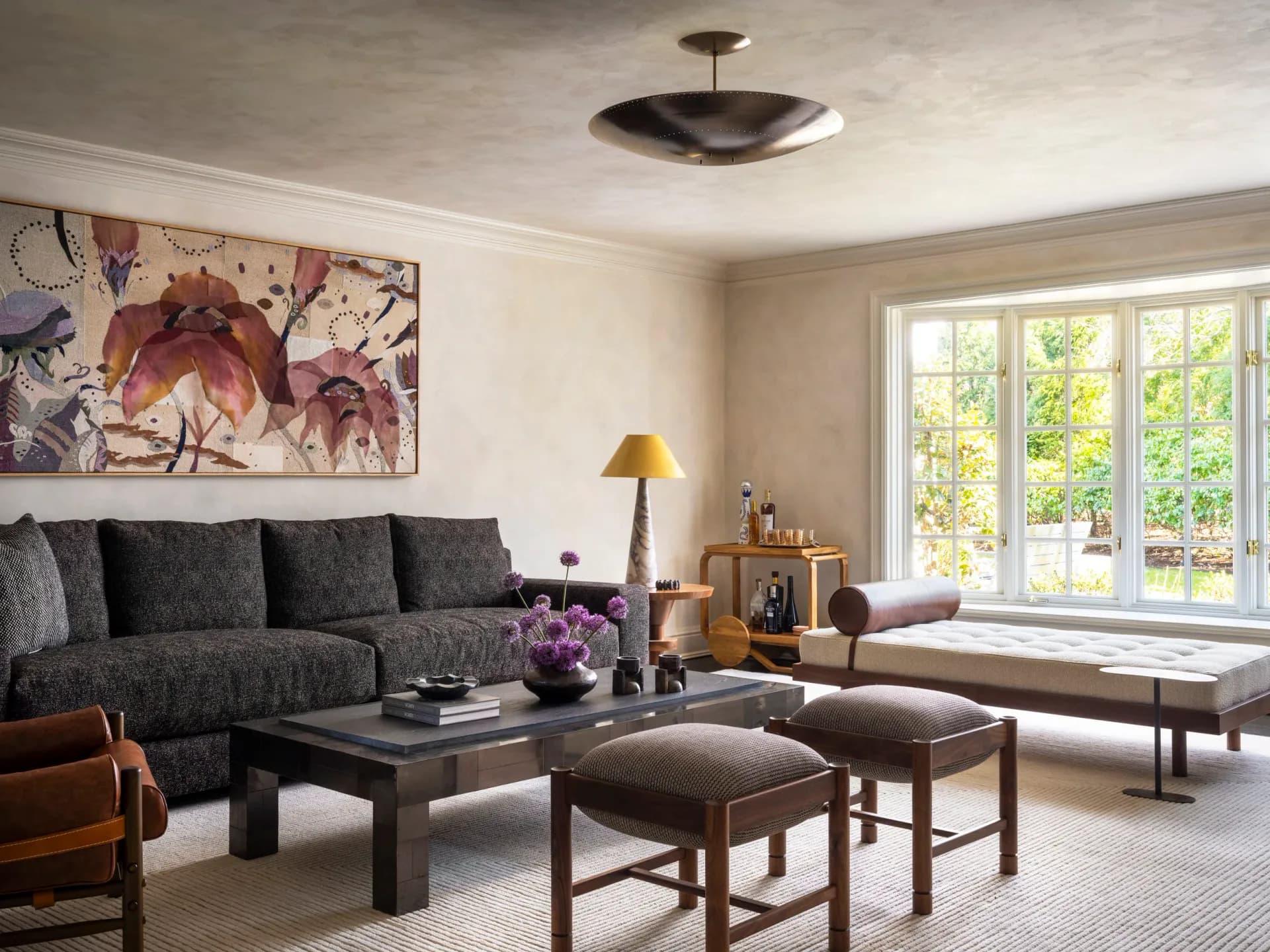 Contemporary living room with charcoal sectional, black coffee table, warm wood accents, floral artwork, and garden views by Diana Litchfield.