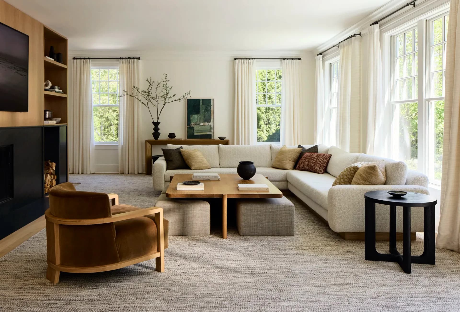Bright living room with cream curved sofa, wooden coffee table, warm accent chairs, and floor-to-ceiling windows with sheer curtains by Diana Litchfield.