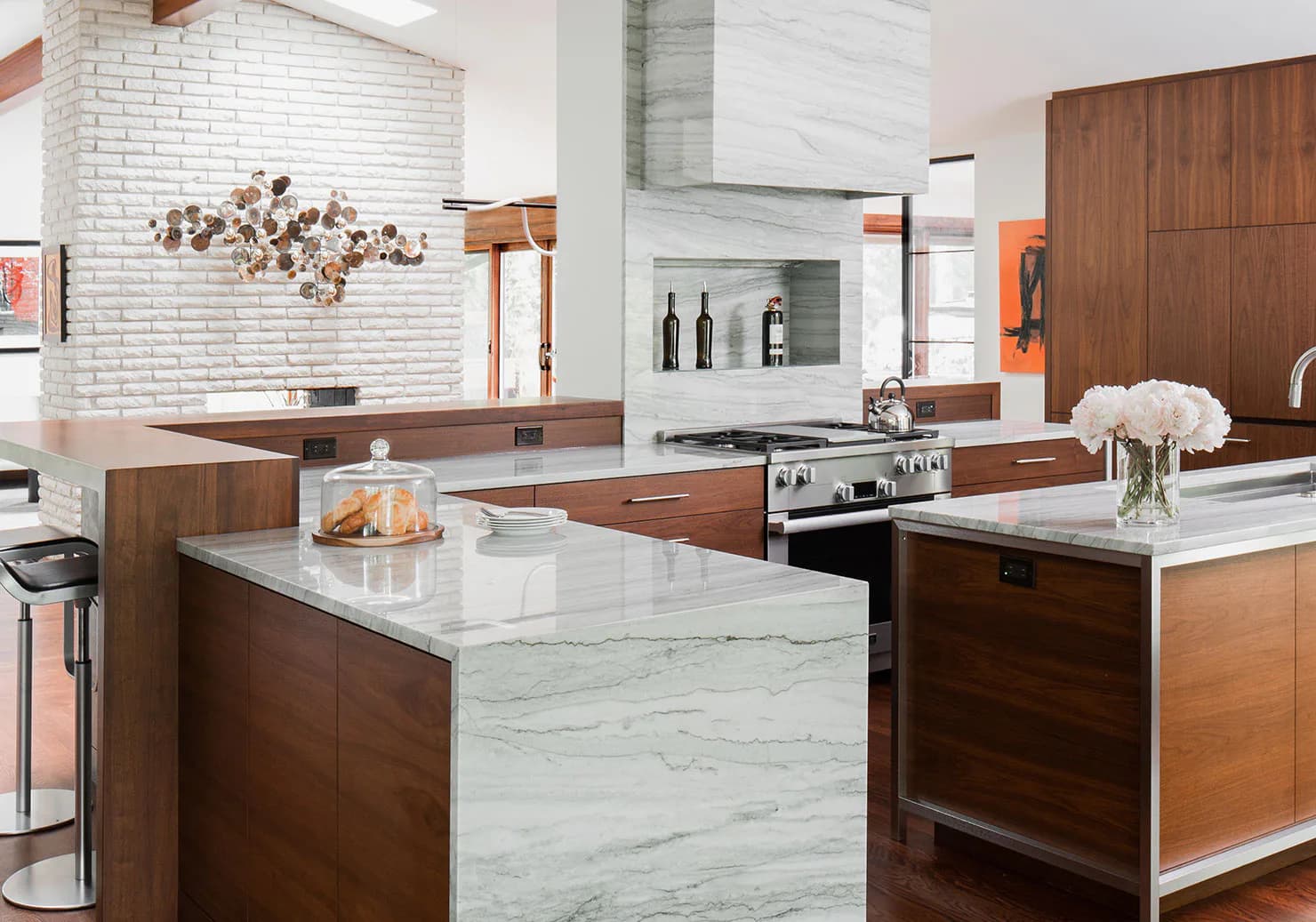 Modern kitchen with warm wood cabinetry, marble waterfall island, white subway tile backsplash, and stainless steel appliances by Diana Reinlein.