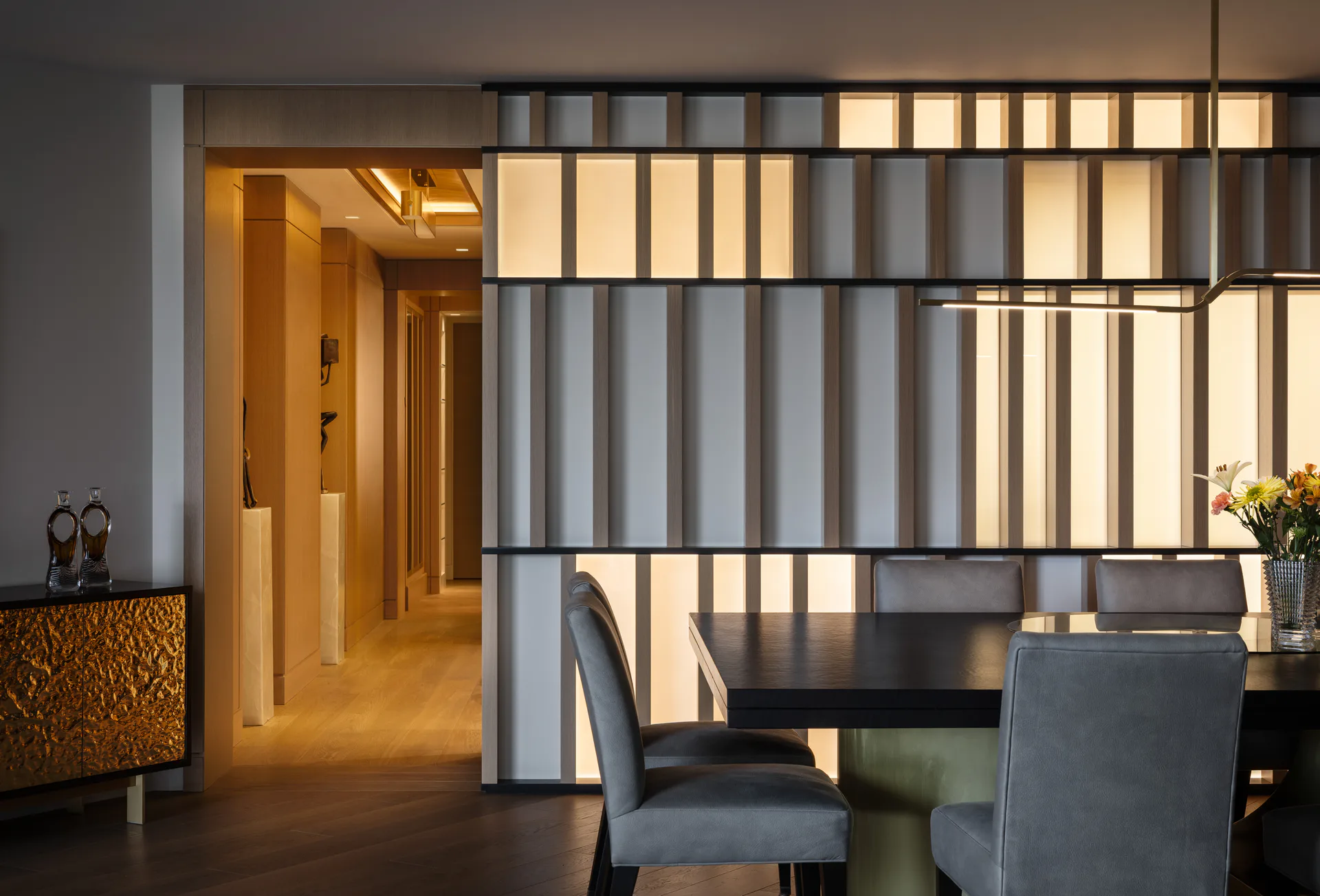 Contemporary dining space with warm wood tones, vertical slatted room divider screening, and modern gray upholstered chairs by Diana Reinlein.