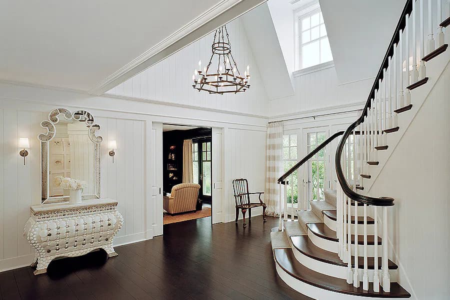 Elegant foyer with curved staircase, decorative console table, pendant chandelier, and polished dark floors by Diana Sawicki.