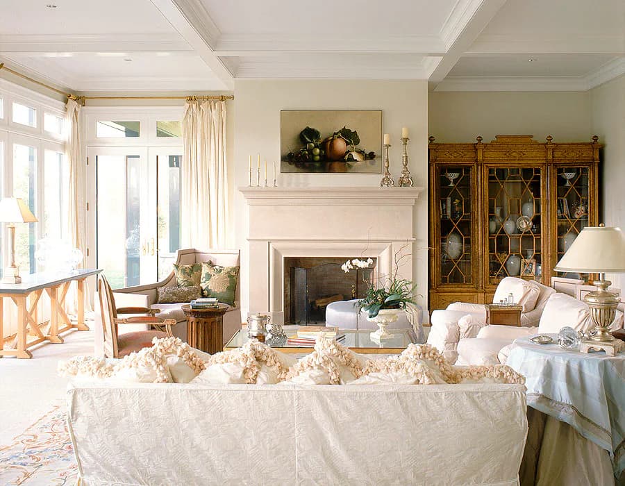 Elegant living room with cream sofa, fireplace, coffered ceiling, and antique wood cabinet, designed by Diana Sawicki.
