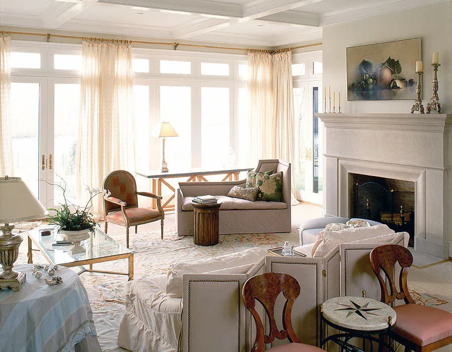 Elegant living room with cream and wood tones, fireplace, large windows with drapes, upholstered seating, and classic furnishings by Diana Sawicki.