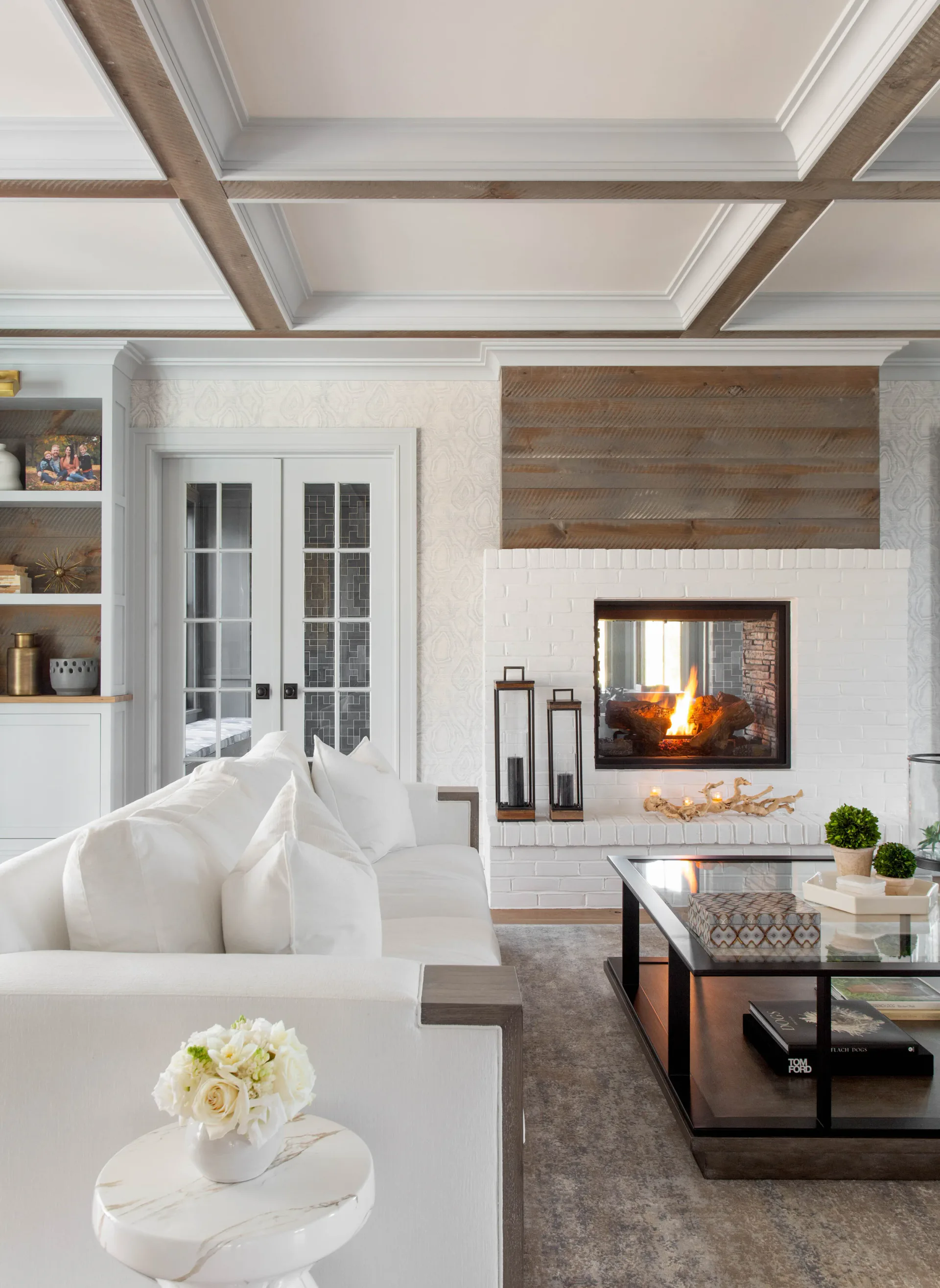 Modern living room with coffered ceiling, white built-ins, fireplace with wood accent wall, and contemporary furnishings by Diane Guariglia.