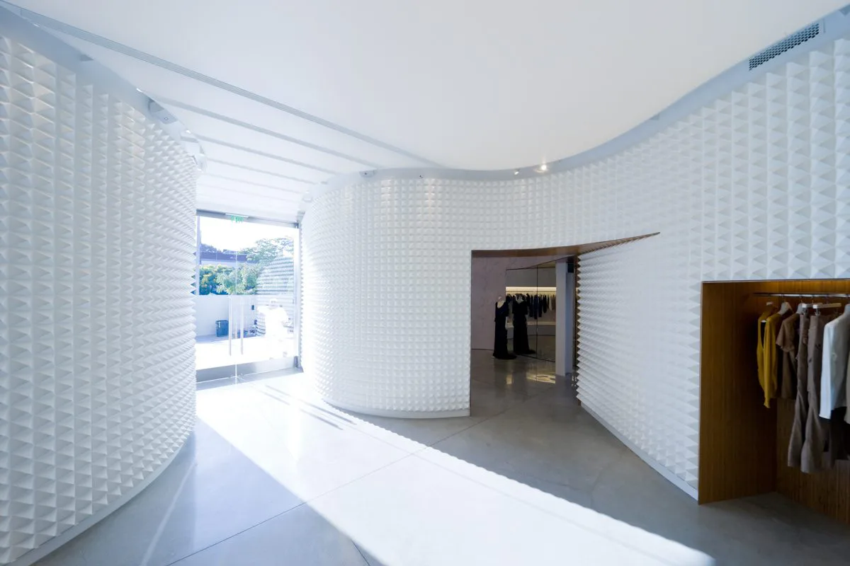 Minimalist retail interior with curved white textured walls, polished concrete flooring, and clothing racks by Dina Reziapova.