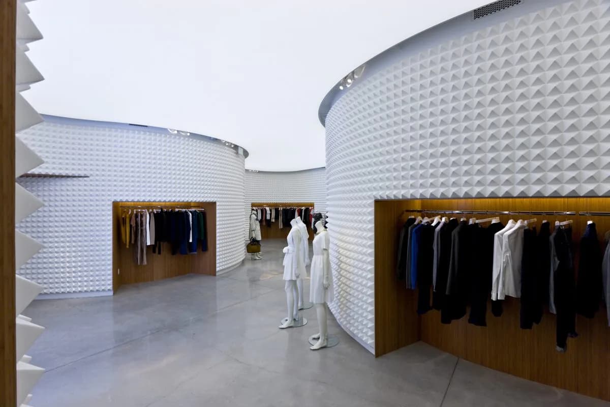 Modern retail clothing boutique with curved white textured walls, wooden display alcoves, and polished concrete flooring by Dina Reziapova.