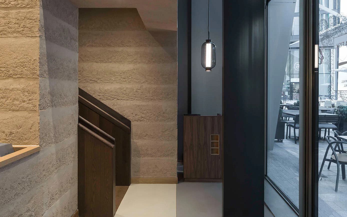 Modern entryway with travertine stone walls, dark wooden door, black framing, and pendant lighting, designed by Ditte Hesse.
