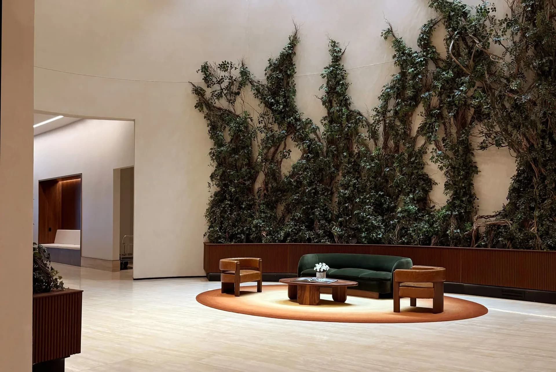 Modern interior lobby featuring a sunken seating area with green upholstered furniture, wooden accents, and a striking living ivy wall installation by Dominic Kozerski.