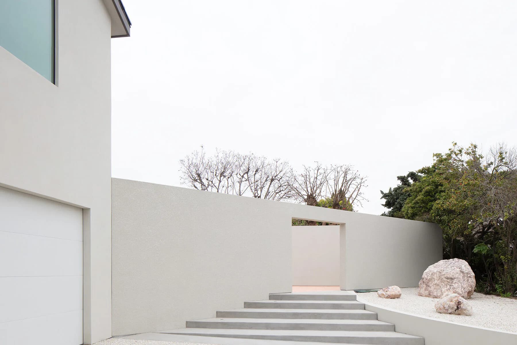 Minimalist white concrete courtyard with stepped platform, sculptural boulder, and clean modernist architecture by Dominic Leong.