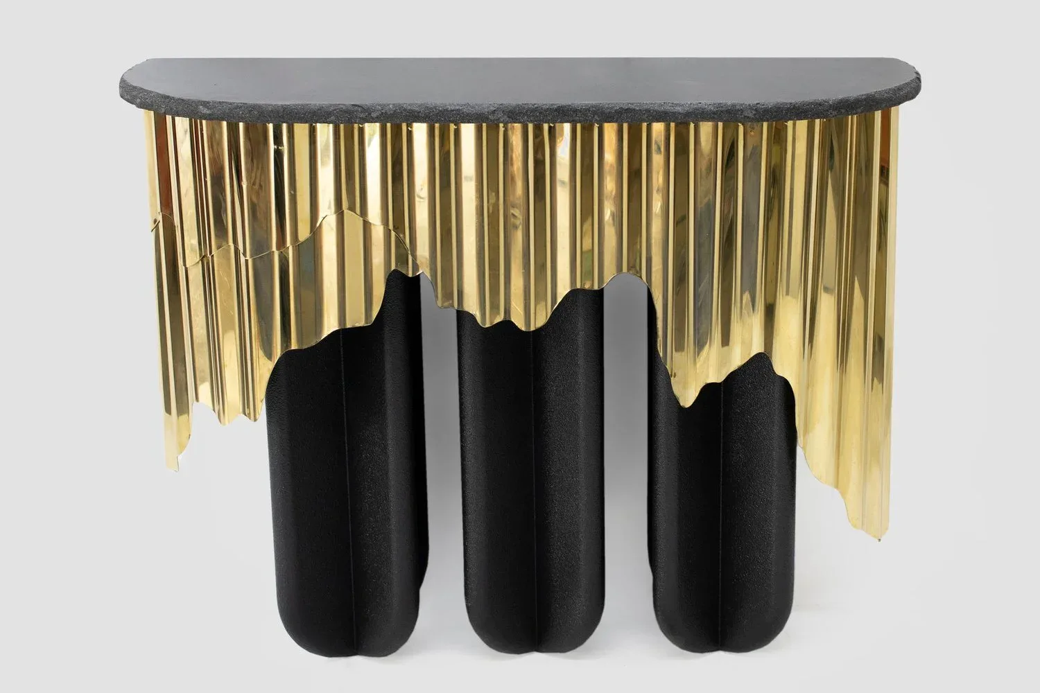 Modern sculptural console table with gray curved top, three black cylindrical pedestals, and cascading gold fringe draping by Dustin John.