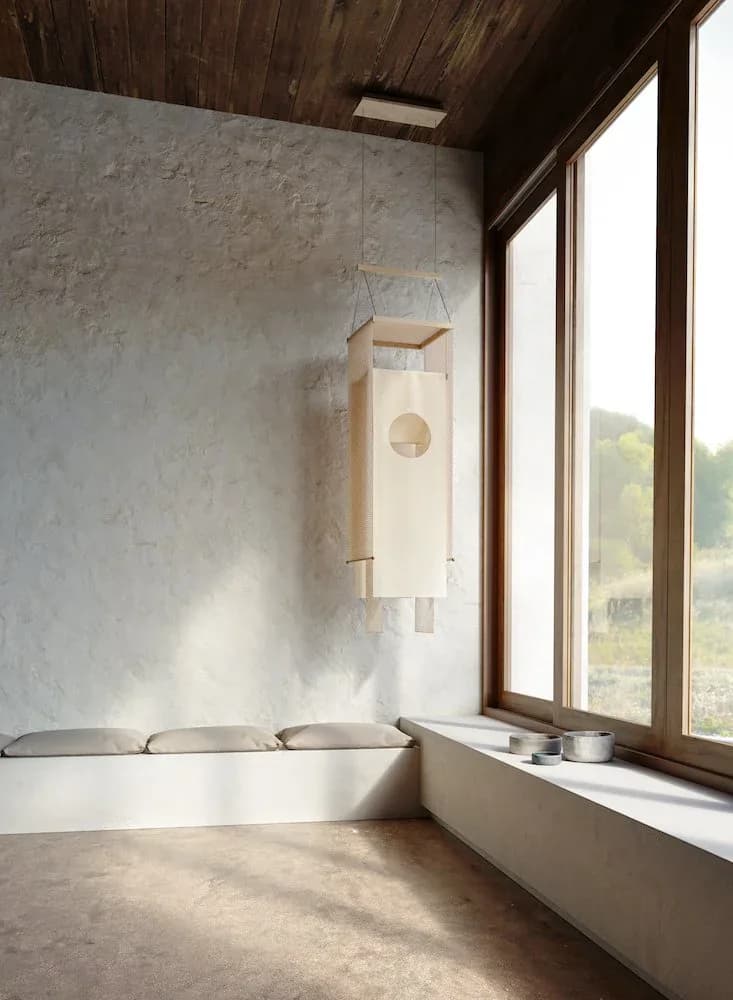 Minimalist interior space with concrete floors, white plaster walls, dark wood ceiling, and large windows overlooking landscape, featuring suspended wooden birdhouse by Dylan Davis.