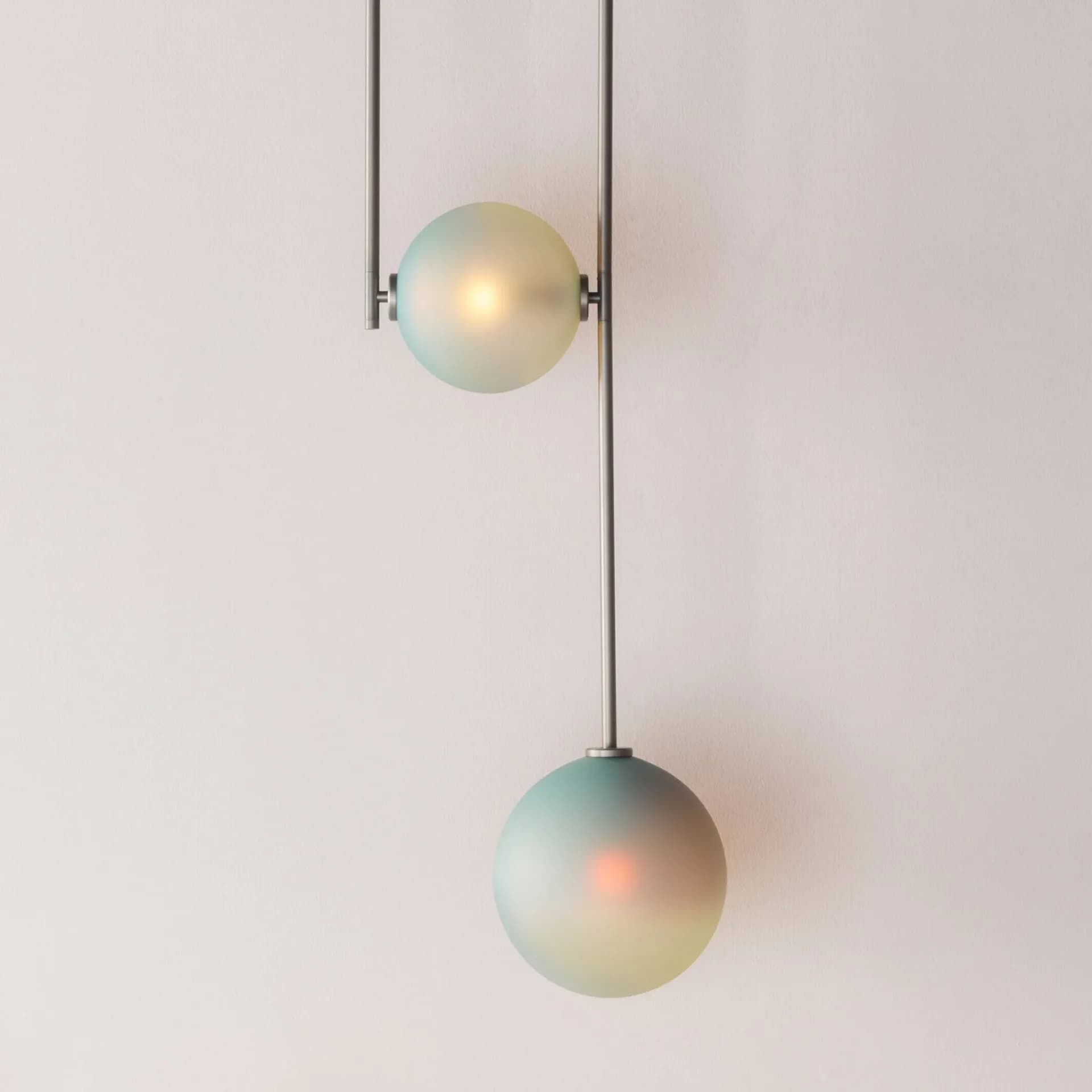 Minimalist pendant lighting installation featuring two frosted glass spheres suspended from thin metal rods against a neutral wall, by Dylan Davis.