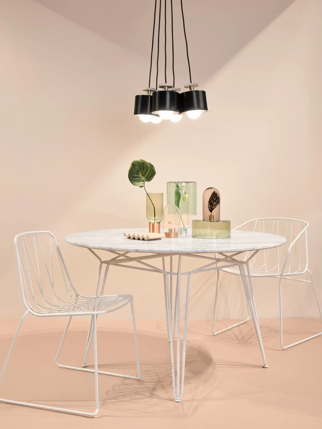 Minimalist dining setup with white wireframe chairs, round white table, and black pendant lights against warm beige walls by Dylan Davis.