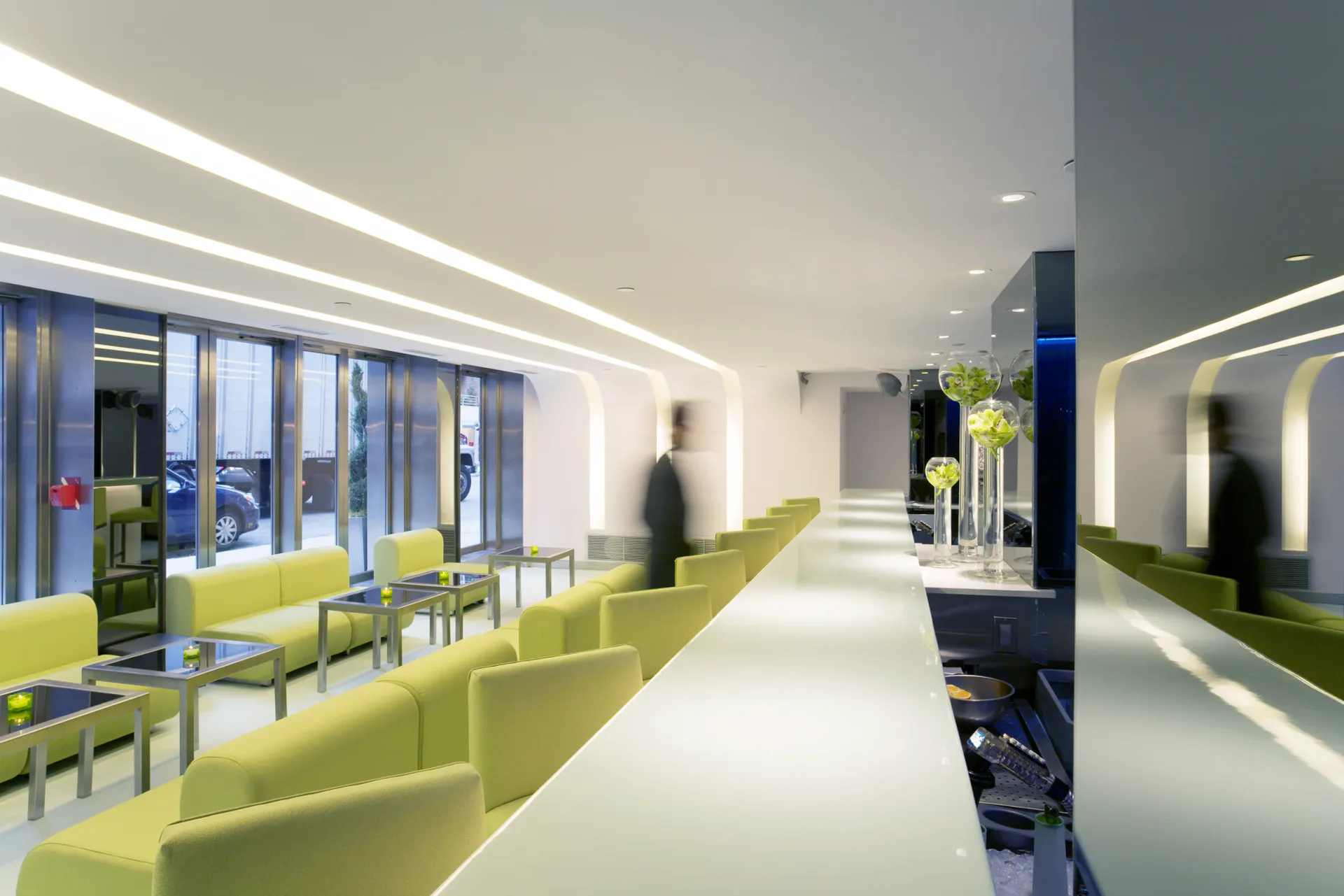 Modern corporate corridor with lime-green seating pods, continuous linear ceiling lights, and floor-to-ceiling windows designed by Ed Kopel.