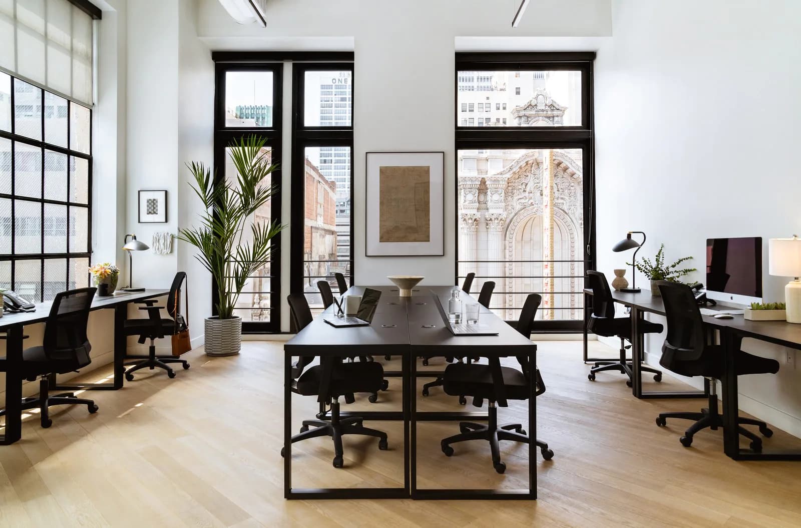 Modern open-plan office with black-framed workstations, light wood flooring, floor-to-ceiling windows, and minimalist furnishings by Elide Rathborne.