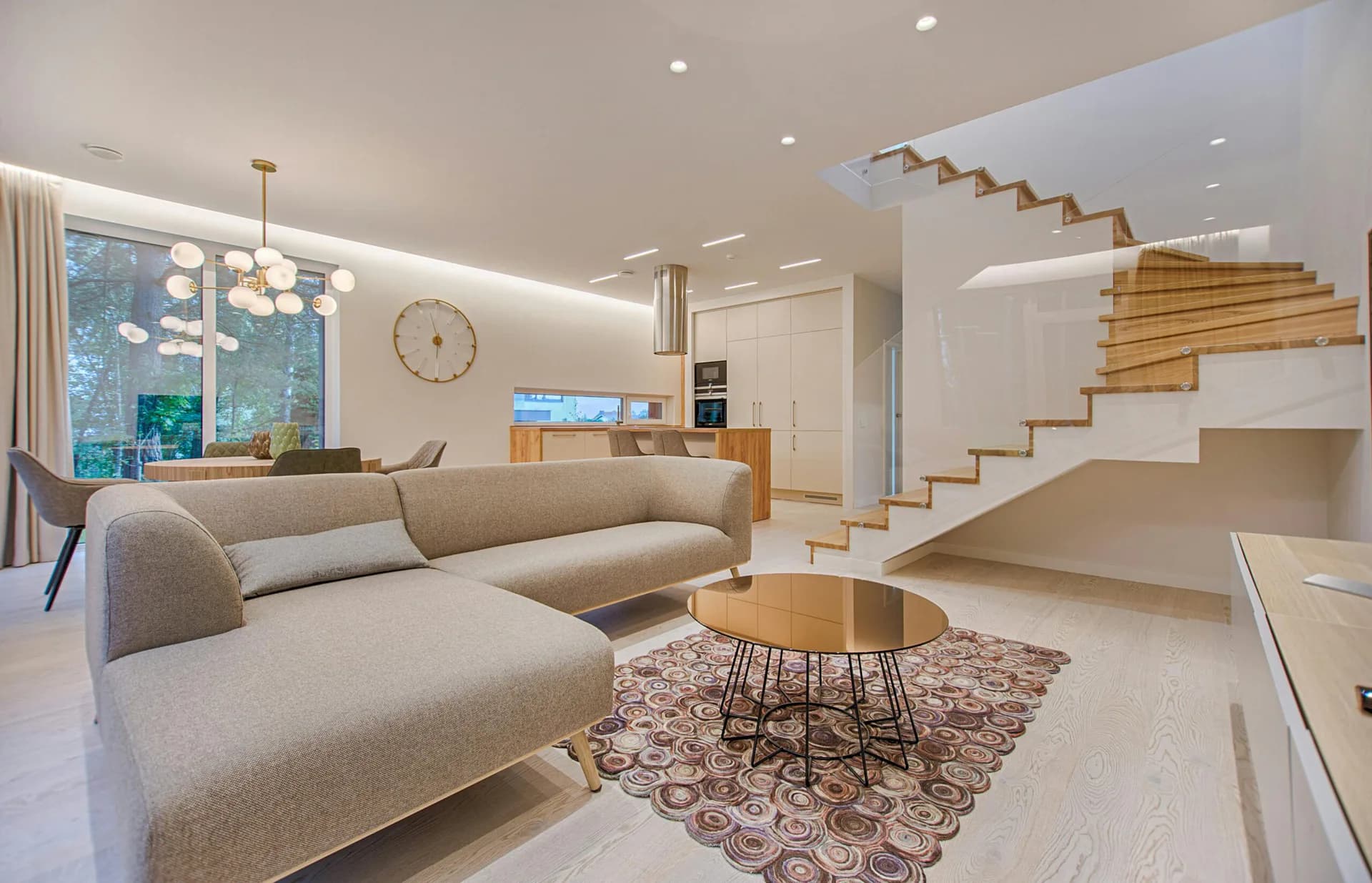 Modern living room with beige sectional sofa, wooden floating staircase, and minimalist décor in warm neutral tones by Elizabeth Leite.