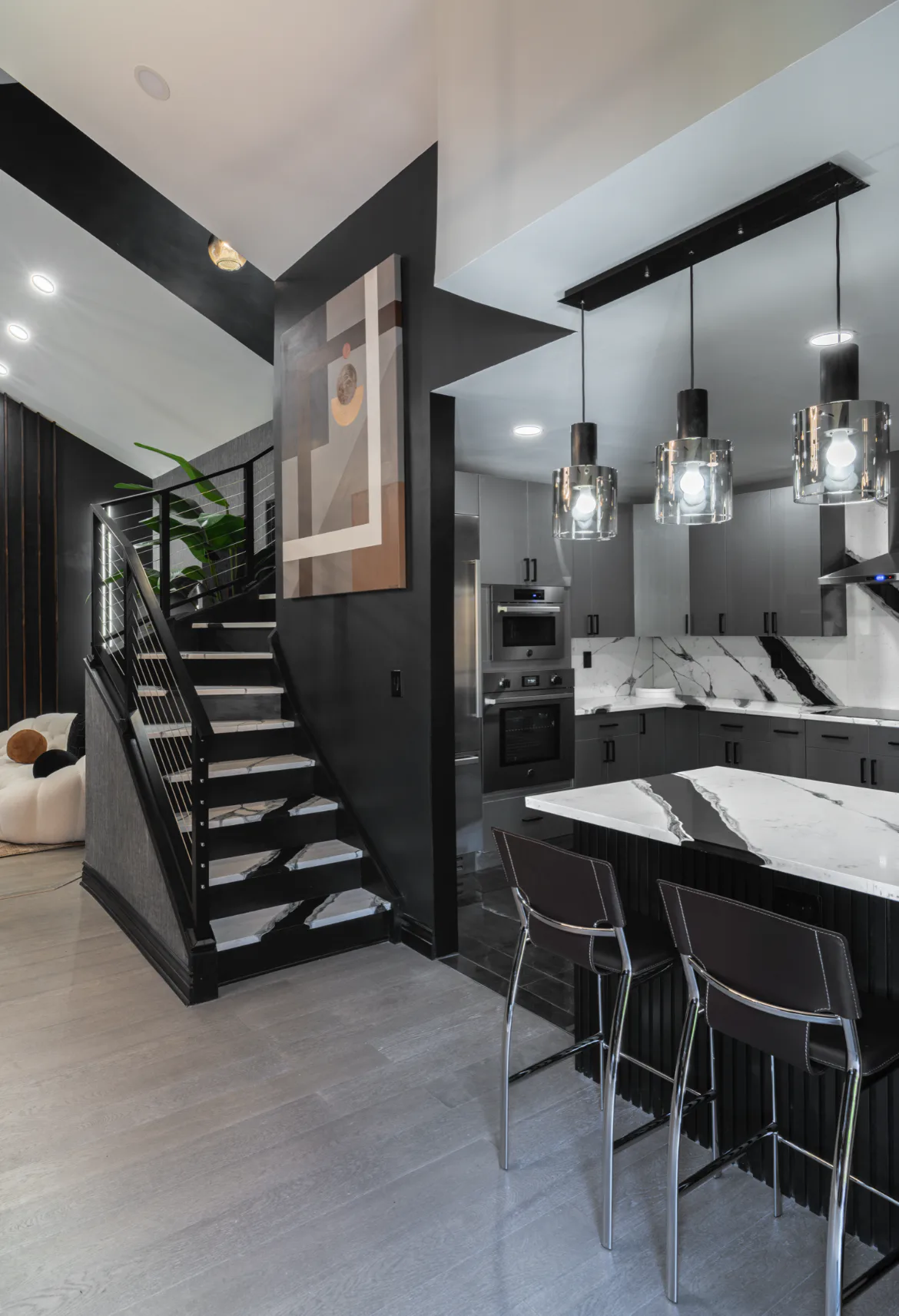 Modern black and white kitchen with marble countertops, pendant lighting, and floating staircase by Elizabeth Leite.