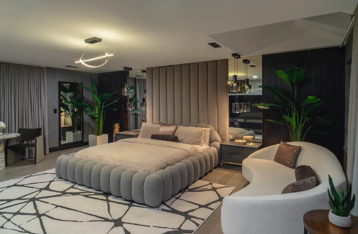 Luxurious modern bedroom with ribbed upholstered headwall, sculptural cloud sofa, warm neutral palette, statement lighting, and lush plants by Elizabeth Leite.