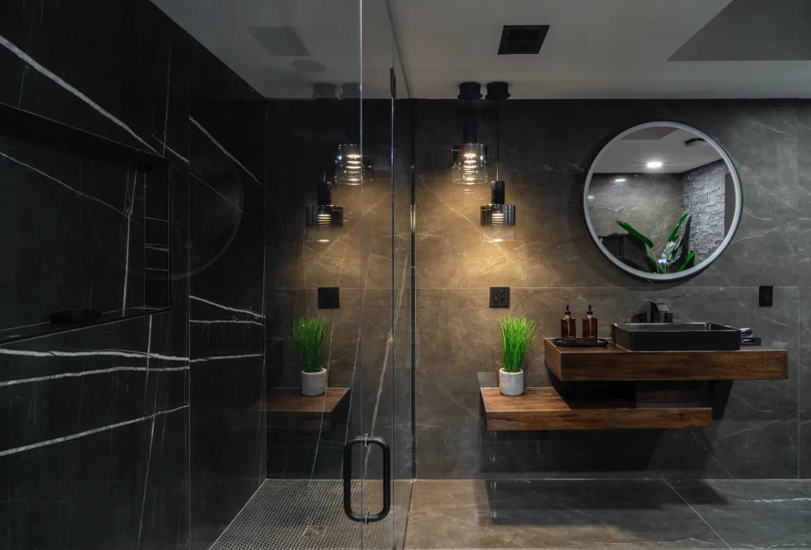 Modern luxury bathroom with black marble walls, wooden vanity, pendant lighting, and walk-in shower by Elizabeth Leite.