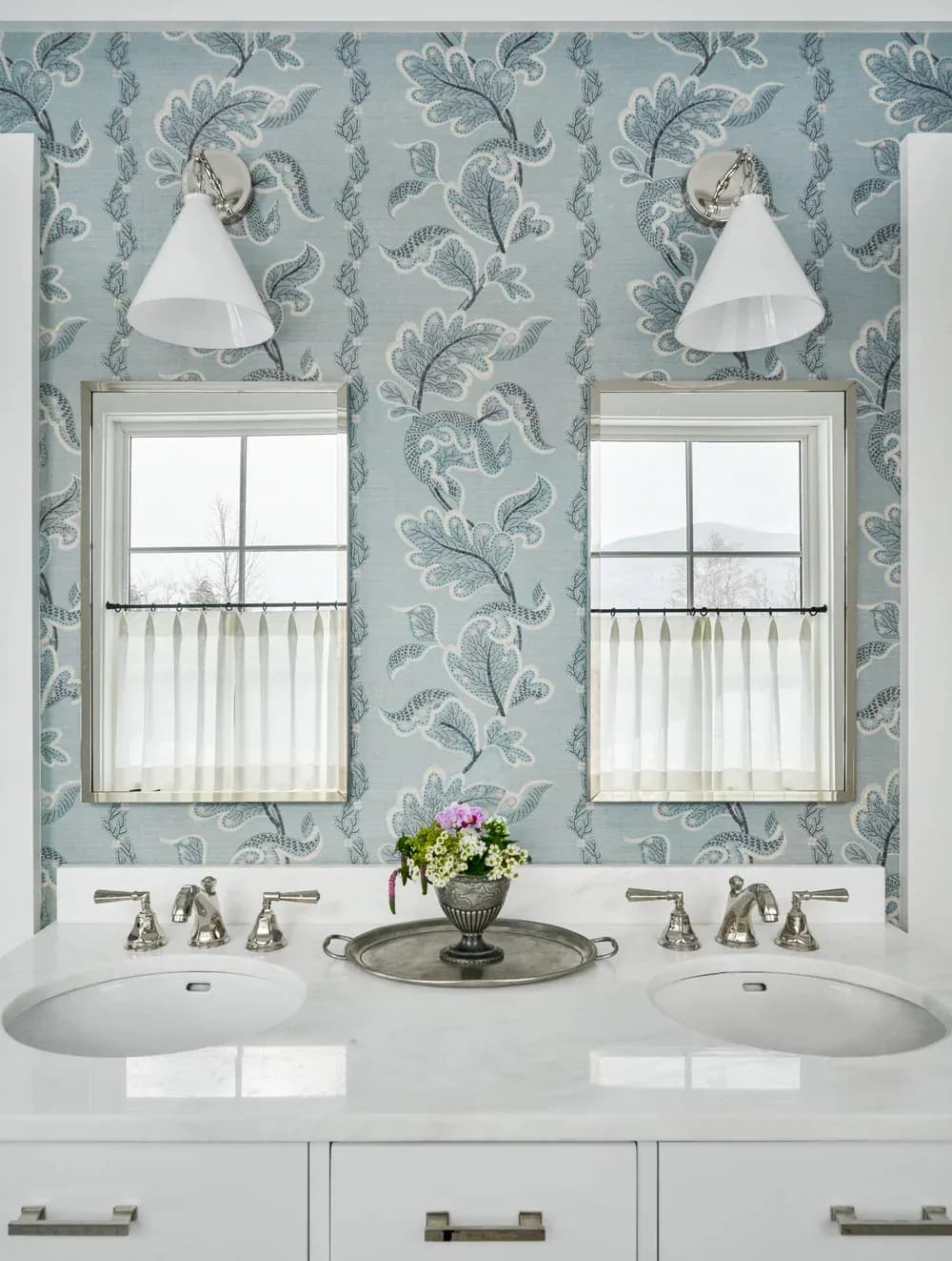 Spa-like bathroom with dual sinks, seafoam damask wallpaper, white sconces, and mirrored windows with sheer curtains by Ellen Marment.