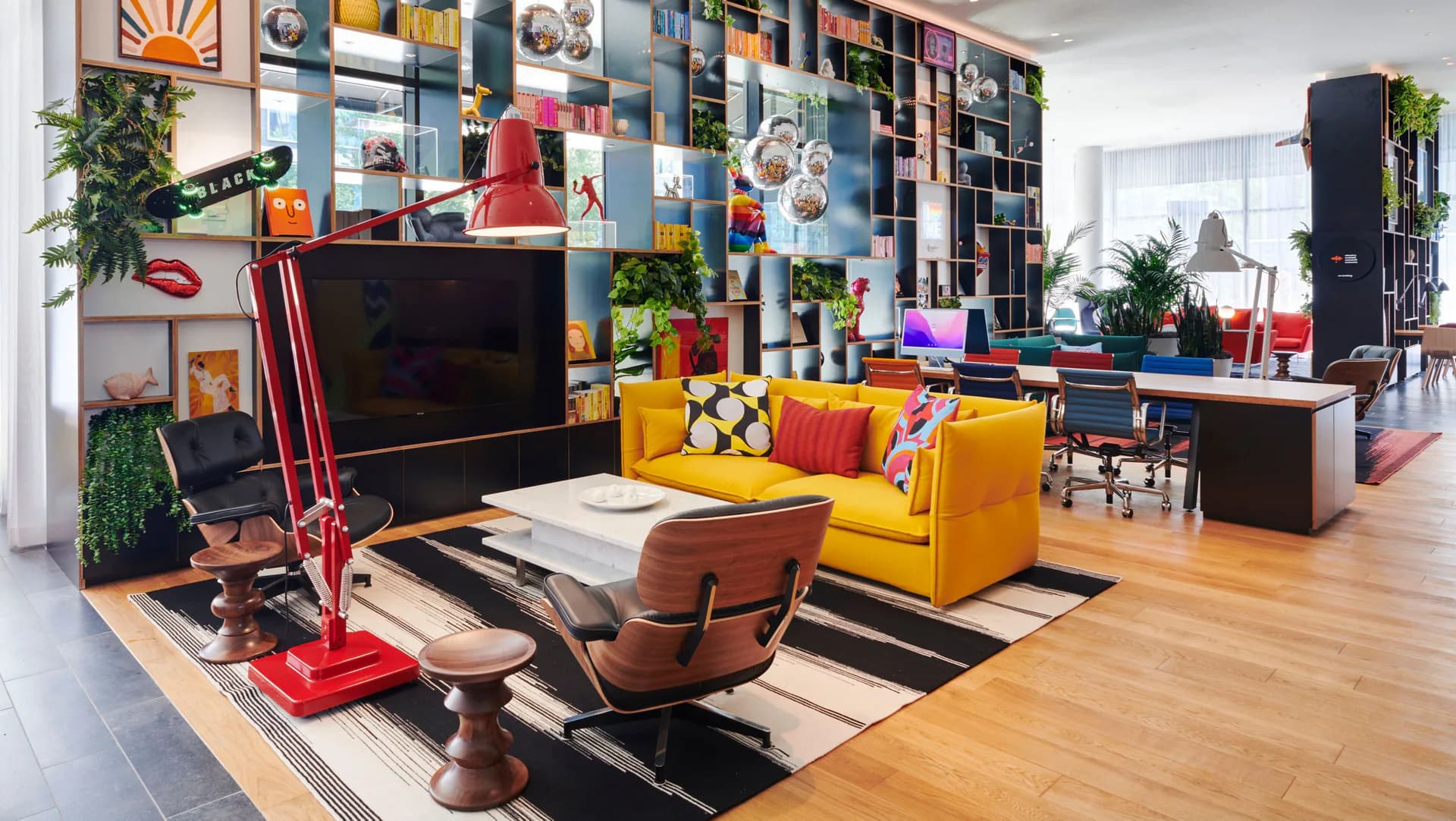 Colorful contemporary living room with yellow sofa, wood flooring, striped area rug, and floor-to-ceiling shelving by Ellen Vega.