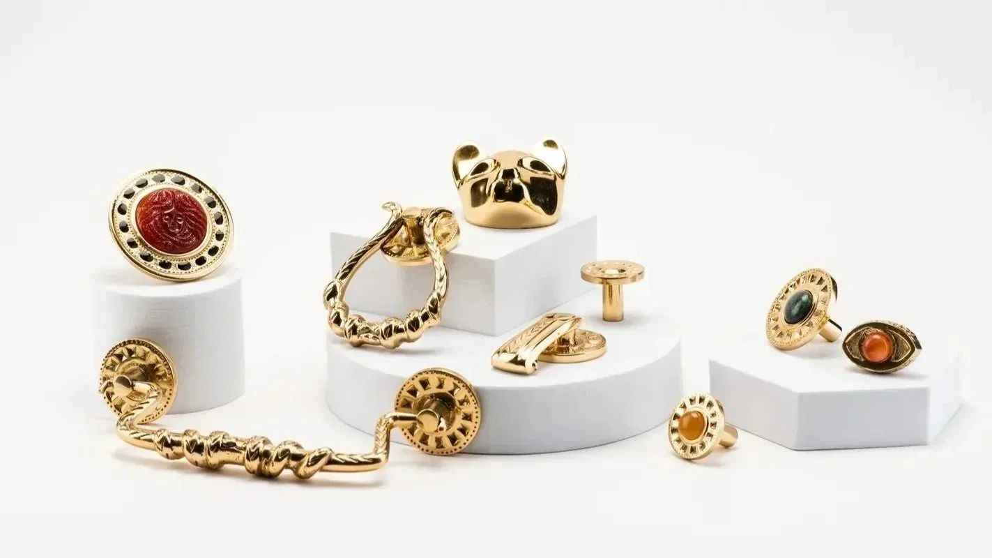 Gold jewelry pieces with gemstone accents arranged on white cylindrical pedestals against a neutral background by Emeryann Hare.
