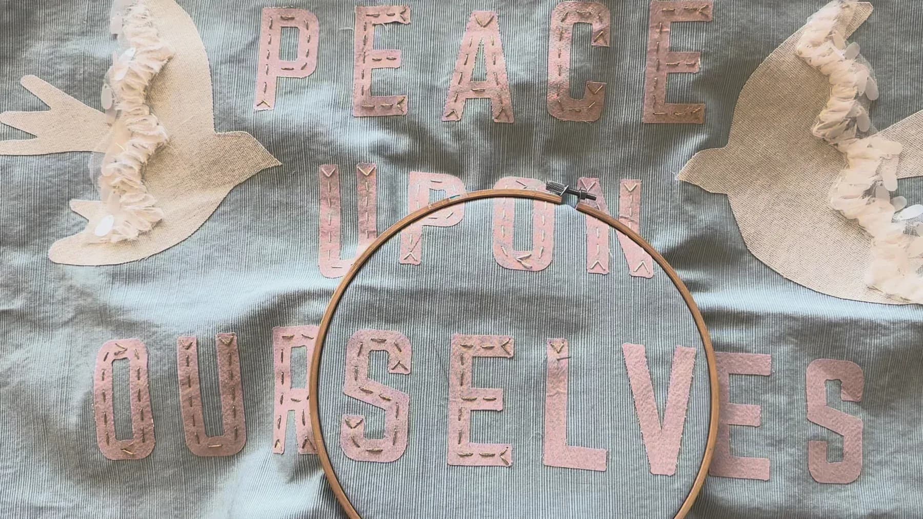 Embroidery artwork featuring dove motifs and text reading 'Peace' and 'Ourselves' on linen with wooden hoop, by Emily Fischer.