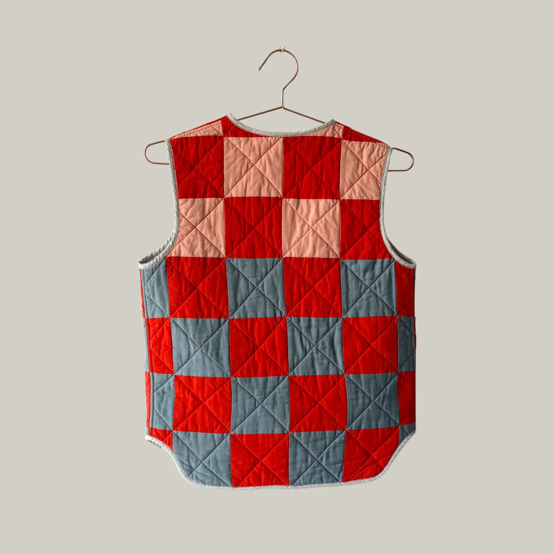Red and blue checkered quilted vest on wooden hanger against neutral background by Emily Fischer.