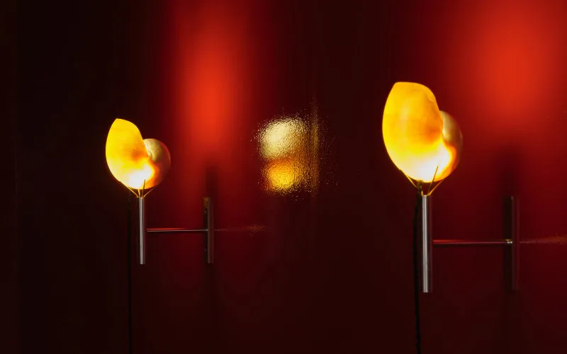 Three illuminated yellow pendant lights suspended against a deep red wall, creating a warm atmospheric lighting installation by Emily Paulson.
