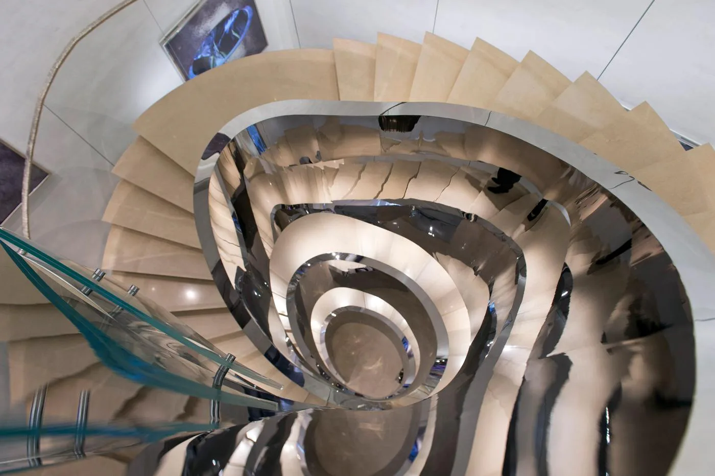 Spiral staircase with cream-colored steps and dark metal railings photographed from above, showing geometric circular pattern descending through multiple floors by Enrique Pincay.