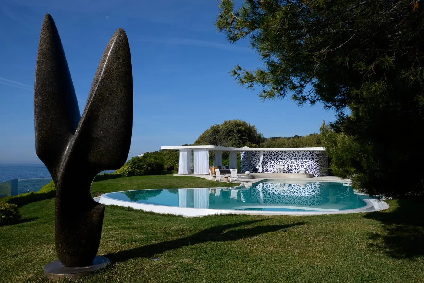 Modern waterfront villa with curved pool, white stone facade, and manicured grounds overlooking the sea, designed by Enrique Pincay.