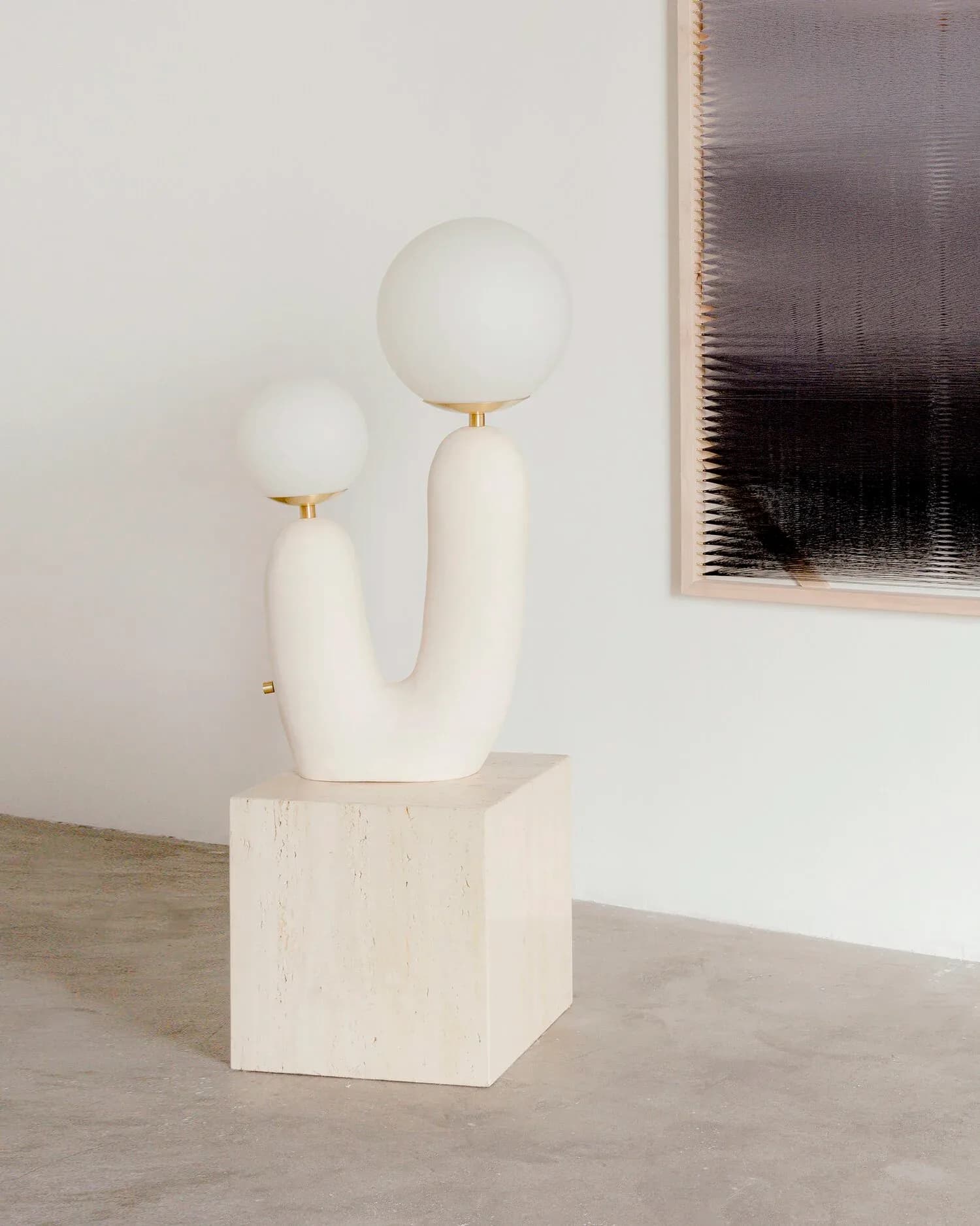 Minimalist sculptural installation featuring white curved forms with spherical tops on a cube base, alongside abstract wall art, by Eny Lee Parker.