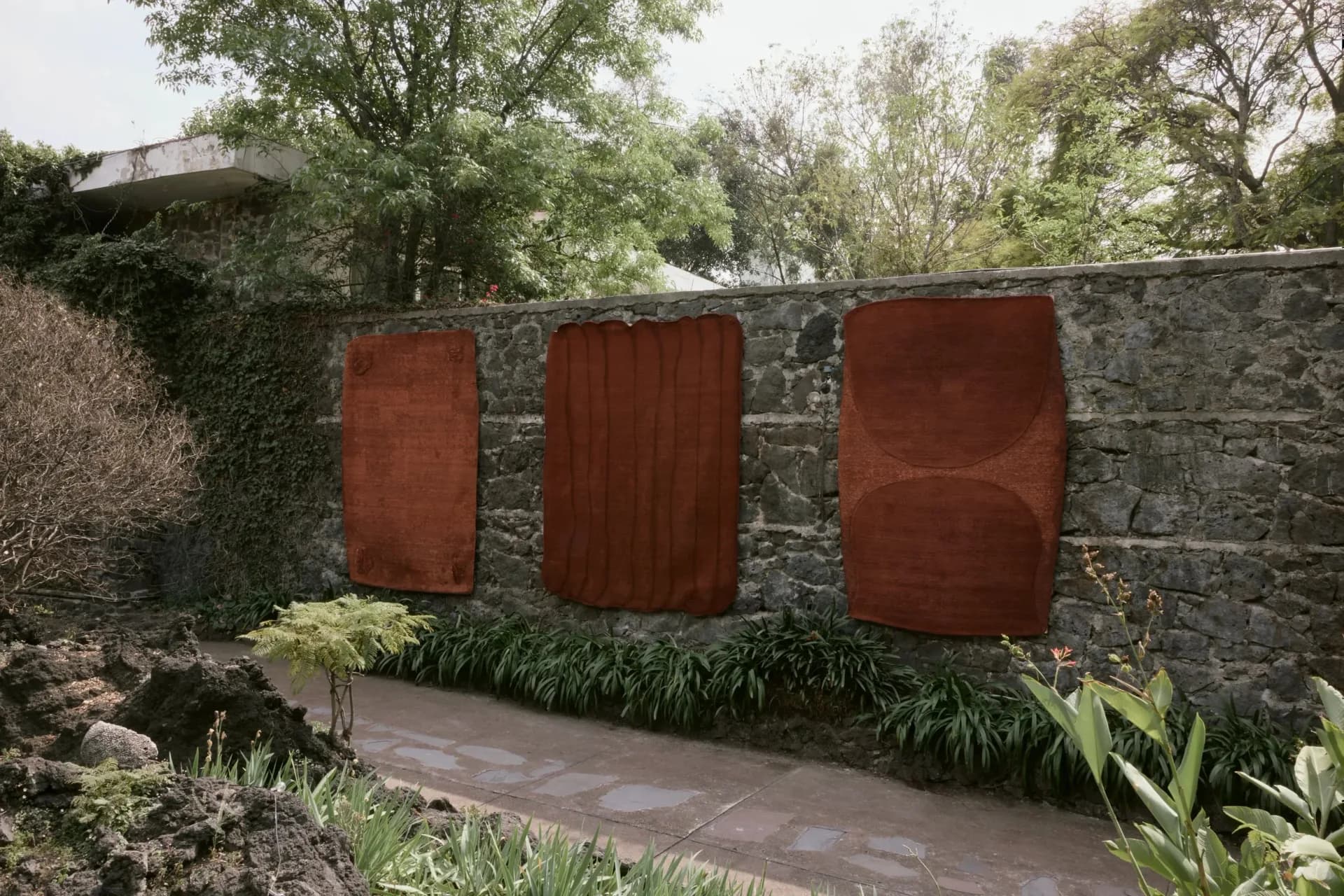 Garden installation featuring three large rusted steel panels set into a stone wall, with lush plantings below, designed by Eny Lee Parker.
