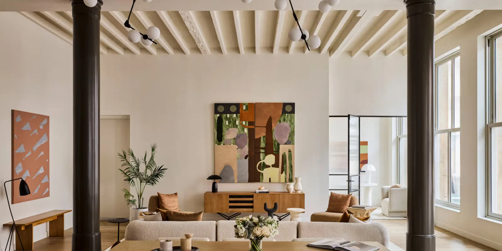 Bright loft interior with concrete columns, white ceiling with exposed beams, mid-century furniture, and large windows, designed by Eran Chen.