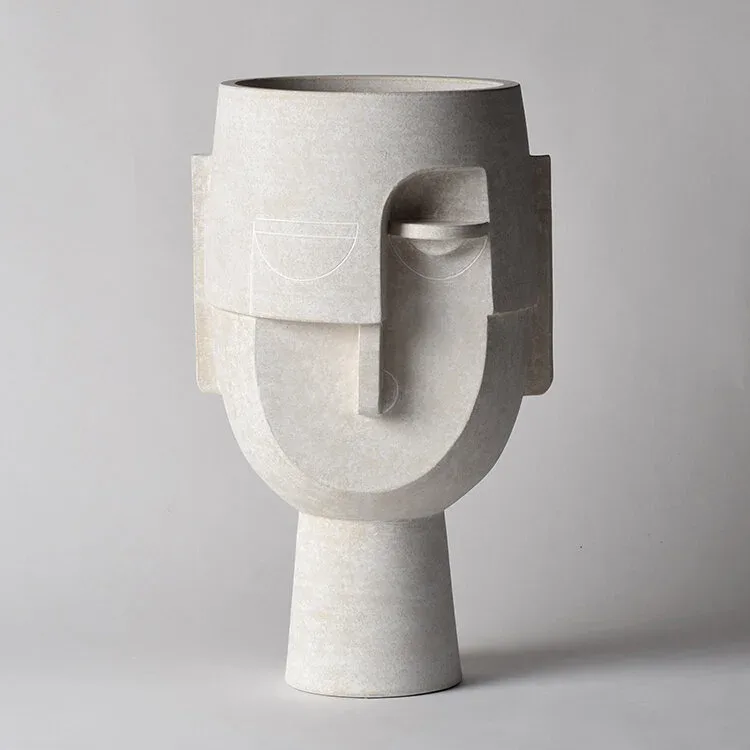 Abstract sculptural vessel in white stone with geometric facial features and cylindrical base, by Eric Roinestad.