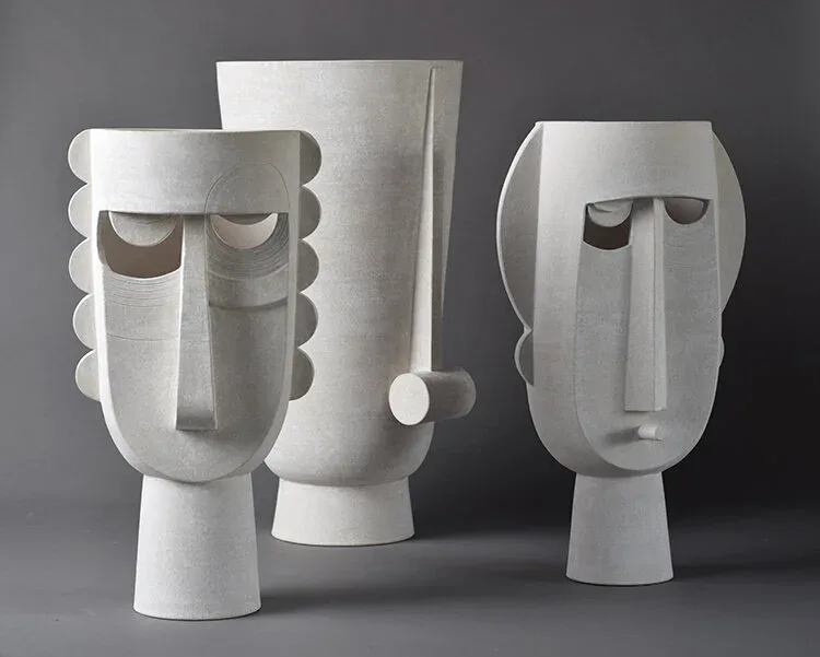 Abstract sculptural white ceramic head forms with geometric features and hollow cavities, arranged as a series of stylized faces by Eric Roinestad.