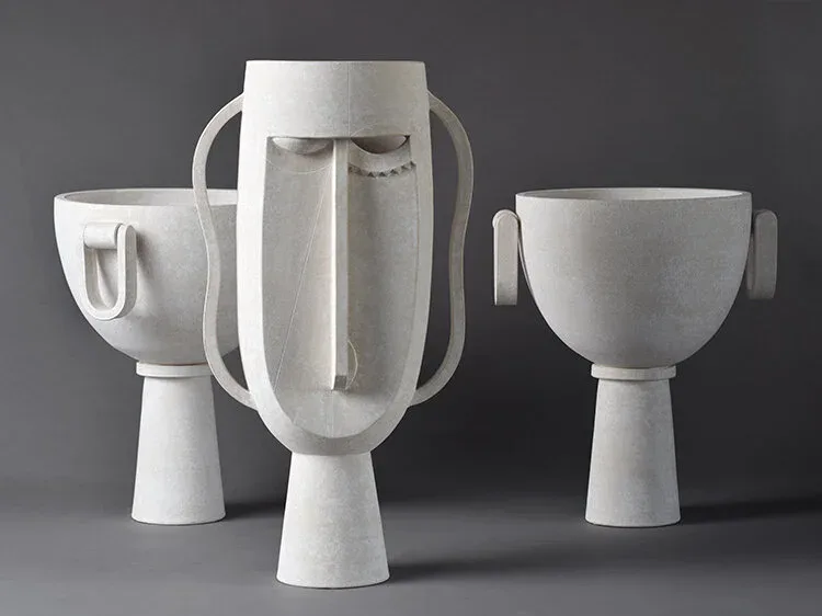 Three white ceramic vessels with geometric forms and cylindrical bases photographed against a gray background, showcasing minimalist design by Eric Roinestad.