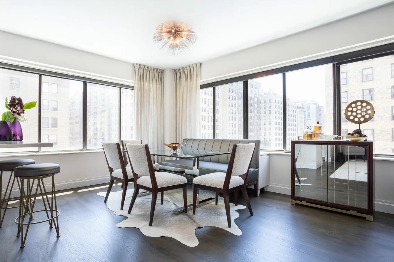 Modern high-rise apartment living room with floor-to-ceiling windows, mid-century furniture, dark wood flooring, and city skyline views, designed by Eric Winnick.