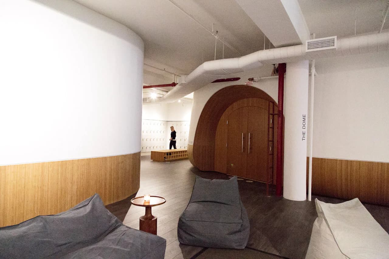 Modern interior space with curved white ceiling elements, wood paneling, dark upholstered seating, and a distinctive arched doorway by Erik Tietz.